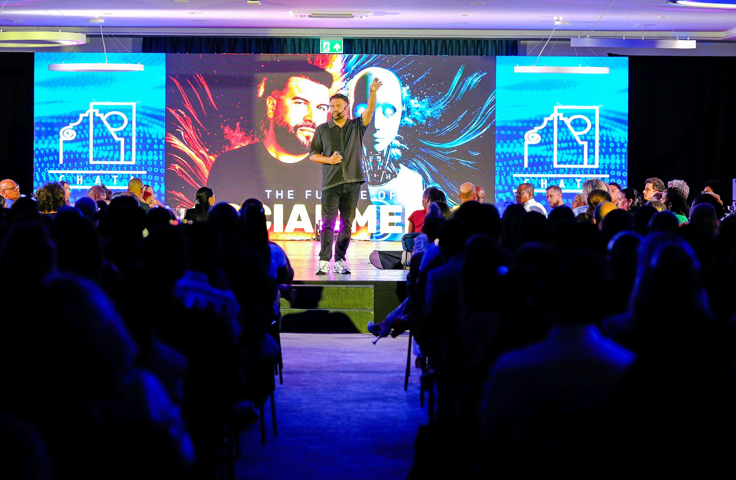 Conferencista en tarima frente a una pantalla LED y un auditorio lleno